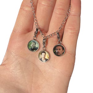 May include: A silver chain necklace with three round glass charms featuring different men's faces.