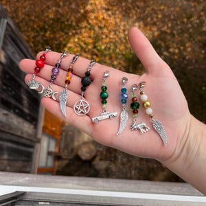 May include: Seven charm bracelets with different colored beads and charms, including a crown, a crescent moon, a pentagram, a car, and a deer. The charms are attached to silver chains.
