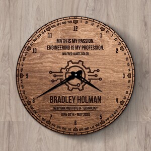 Op de afbeelding: Een ronde houten klok met een donkerbruine afwerking. De wijzerplaat toont de tekst "MATH IS MY PASSION. ENGINEERING IS MY PROFESSION." en de naam "BRADLEY HOLMAN." Het heeft een tandwiel- en printplaatontwerp.
