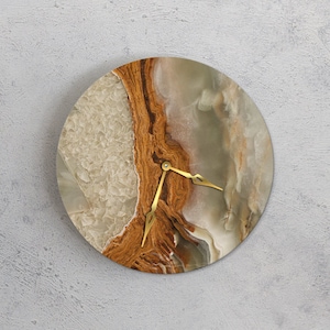 May include: Circular wall clock with a natural stone face. The clock face has beige, brown, and grey tones with gold-coloured hands. The clock is mounted on a light grey wall.