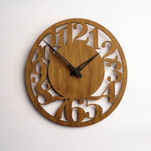 Puede incluir: Un reloj de pared redondo de madera con acabado de madera natural. La esfera del reloj presenta n&uacute;meros recortados y manecillas negras. El reloj tiene aproximadamente 30 cm de di&aacute;metro.