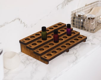 May include: A tiered, wooden essential oil display stand with multiple holes for holding small bottles. The stand is stained a warm brown color and holds several small glass bottles with colored liquids. A gold wire basket is in the background.