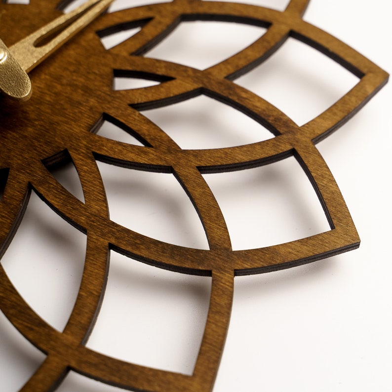 Puede incluir: Un reloj de pared de madera marr&oacute;n oscuro con un dise&ntilde;o calado decorativo. El reloj presenta manecillas doradas y un patr&oacute;n geom&eacute;trico, creando una est&eacute;tica moderna. El dise&ntilde;o del reloj es una serie de l&iacute;neas curvas que se cruzan.