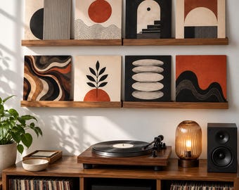 May include: Eight square art prints with abstract geometric, organic, and wave patterns in black, white, and terracotta tones are displayed on two wooden wall shelves above a wooden record player console with a turntable and speakers.