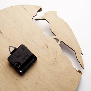 May include: A wooden wall clock with a cutout design of a bird perched on a branch. The clock face is light brown, and the clock mechanism is black. The clock has a unique, natural aesthetic.