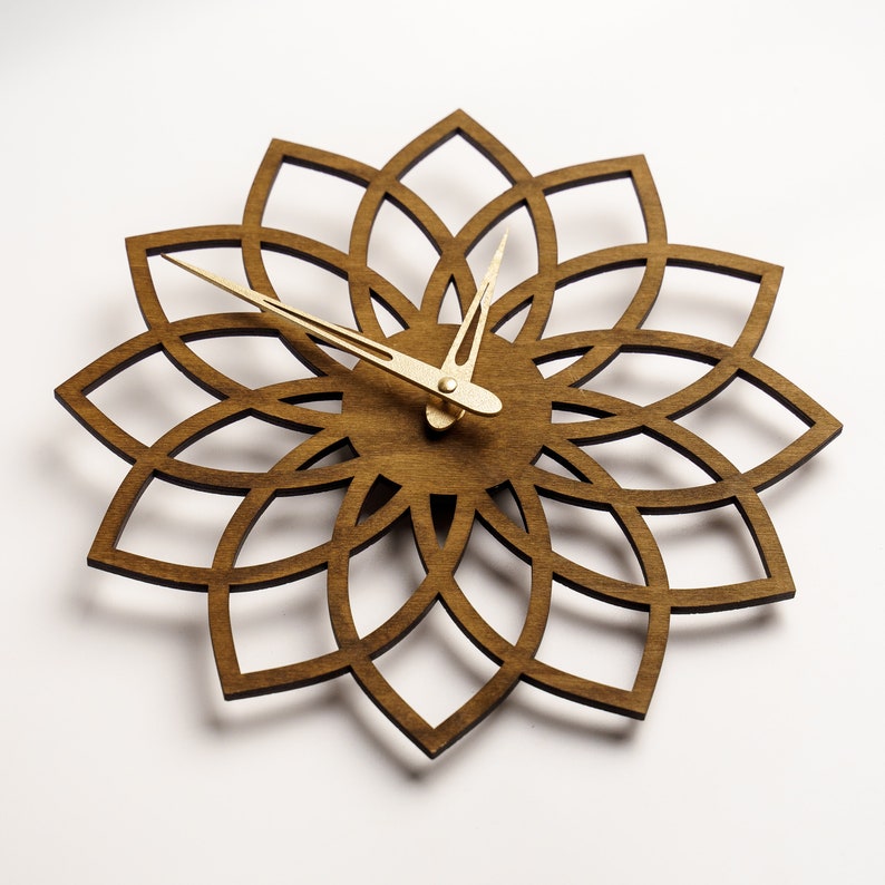 Puede incluir: Un reloj de pared de madera con un dise&ntilde;o floral. El reloj presenta un marco de madera marr&oacute;n oscuro cortado con l&aacute;ser en forma de flor. Las manecillas del reloj son de color dorado. El reloj tiene aproximadamente 30 cm de di&aacute;metro.