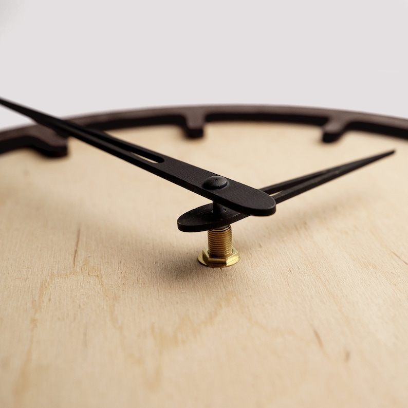 May include: Close-up of a wooden clock face with black hands. The clock has a light wood grain background and a dark brown frame. The minute and hour hands are black and point to the time. The clock's brass center post is visible.