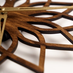 K&ouml;nnte beinhalten: Nahaufnahme einer Wanduhr aus Holz mit dunkelbraunem Finish und dekorativem, durchbrochenem Design. Die Uhr hat goldfarbene Metallzeiger und eine kreisf&ouml;rmige Form, ideal f&uuml;r die Inneneinrichtung.