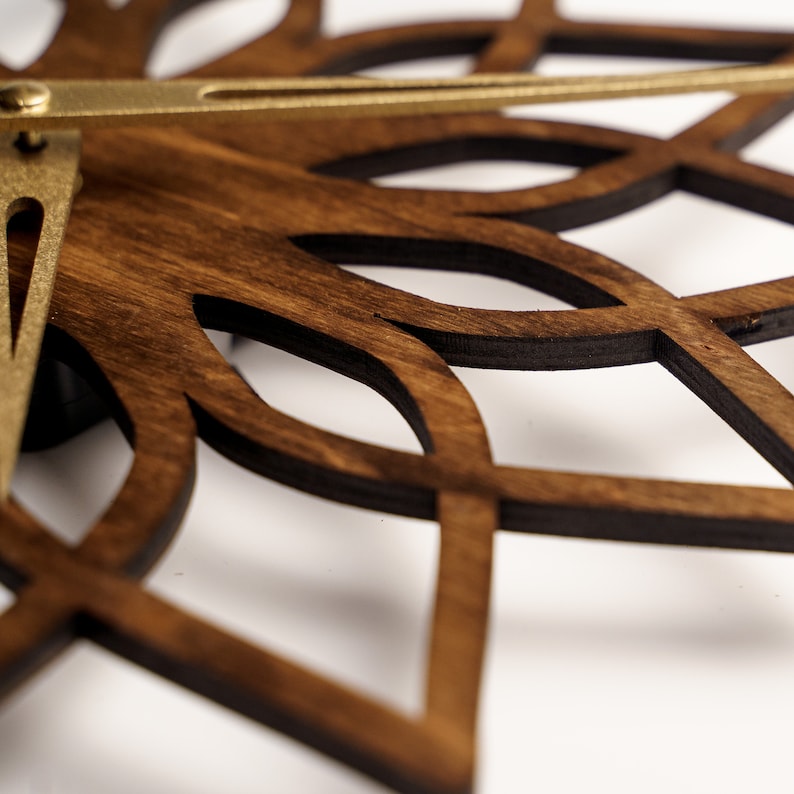 K&ouml;nnte beinhalten: Nahaufnahme einer Wanduhr aus Holz mit dunkelbraunem Finish und dekorativem, durchbrochenem Design. Die Uhr hat goldfarbene Metallzeiger und eine kreisf&ouml;rmige Form, ideal f&uuml;r die Inneneinrichtung.