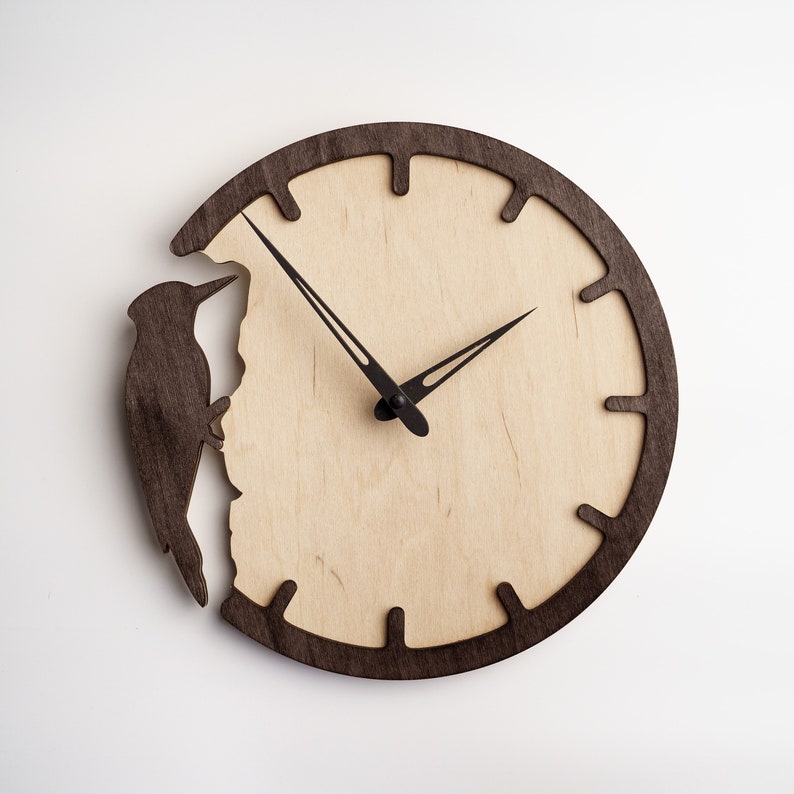 May include: A round wooden wall clock with a light wood face and a dark brown wooden frame. A dark brown woodpecker silhouette is on the left side. The clock hands are black.