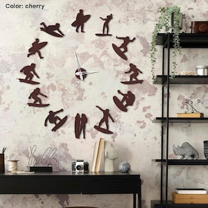 May include: Cherry-coloured wall clock with a unique design of surfers in various poses around the clock face. The clock hands are white, and the overall theme is a modern, sporty aesthetic. The clock is mounted on a textured wall.