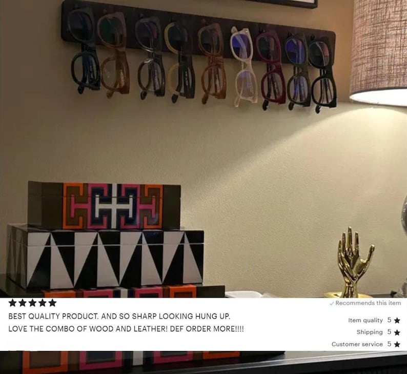 May include: A dark wooden rack displays a collection of eyeglasses with various frame colors. Below, stacked decorative boxes feature geometric patterns in black, white, and vibrant hues. A gold hand sculpture adds a touch of elegance.