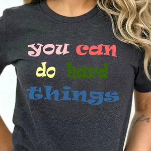 May include: A dark grey t-shirt with the text "you can do hard things" in colorful letters.