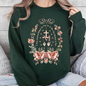 May include: A forest green sweatshirt with a floral design and the text "Pray for Us Who Have Recourse to Thee" in a gold font.