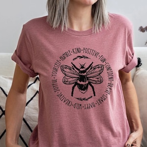 May include: A pink t-shirt with a black bee graphic and the text "Live Joyful Yourself - Humble - Kind - Positive - Fun - Confident - Brave - Smart - Happy - Wild - Creative".