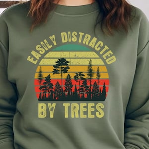 May include: Green sweatshirt with a retro-style graphic that says "Easily Distracted By Trees". The graphic features a sunset with a forest silhouette.