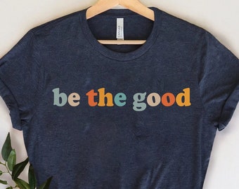 May include: A dark blue t-shirt with the text "be the good" in rainbow colors. The text is in a retro font style.