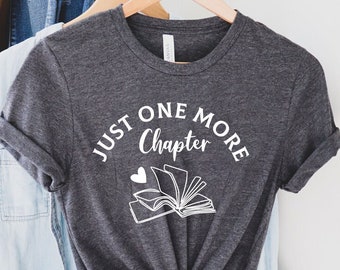 May include: A dark gray t-shirt with the text "Just One More Chapter" and a drawing of a book with a heart above it.
