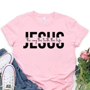 Pu&ograve; includere: Maglietta rosa con testo nero che dice "JESUS the way the truth the life".