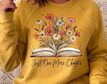 May include: A mustard yellow sweatshirt with a graphic of an open book with flowers growing out of it. The text "Just One More Chapter" is printed below the book.
