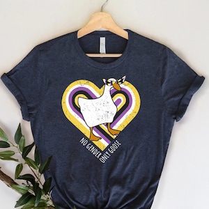 May include: A dark blue t-shirt with a white goose wearing a purple and yellow headband inside a yellow, purple, and white heart. The text "NO GENDER ONLY GOOSE" is below the heart.