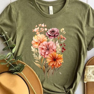 May include: A green t-shirt with a floral print featuring orange, pink, and red flowers. The flowers are arranged in a bouquet and have a watercolor effect.