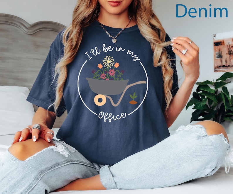 Op de afbeelding: Een marineblauw t-shirt met een witte afbeelding van een kruiwagen vol bloemen. De tekst "I'll be in my office" staat op het shirt gedrukt.
