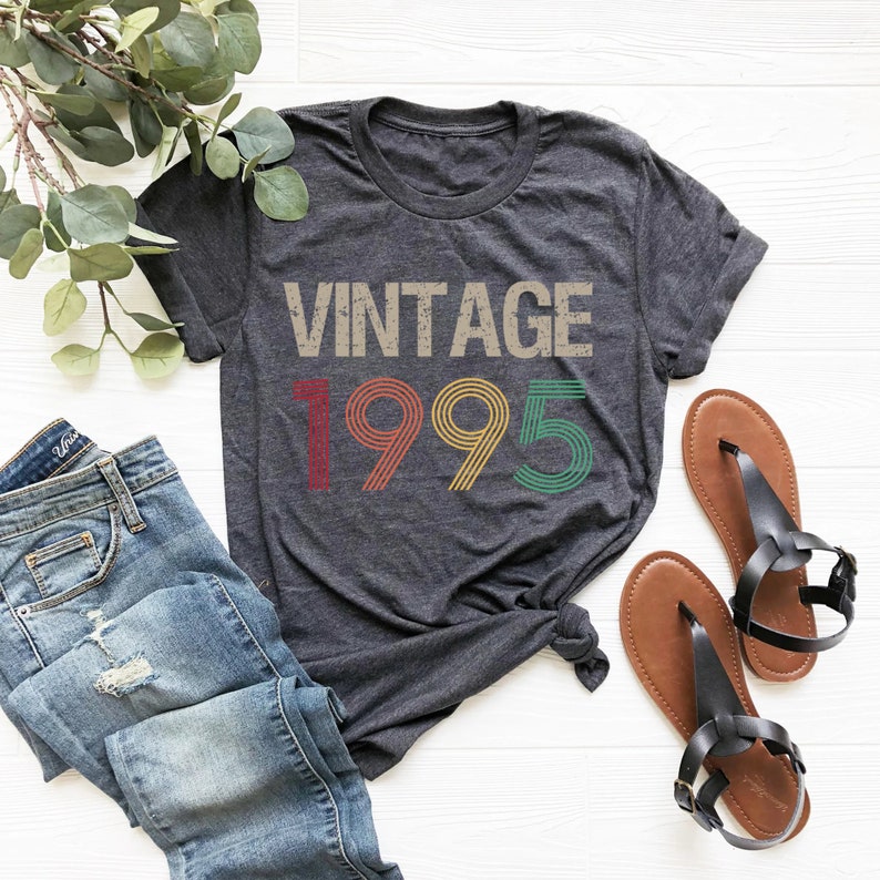 May include: A dark grey t-shirt with the text "Vintage 1995" in rainbow colors. The numbers are stylized with a retro look.