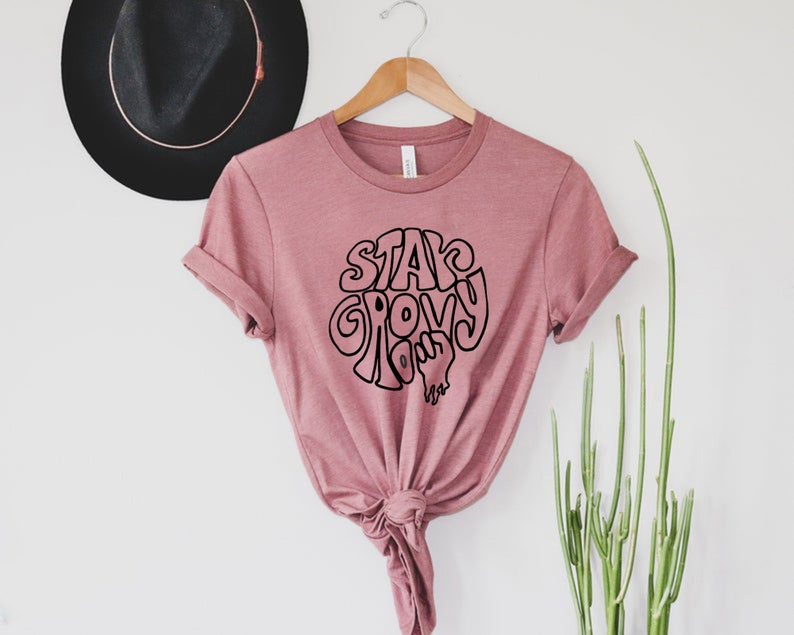 May include: A pink t-shirt with the text "Stay Groovy" in black lettering.
