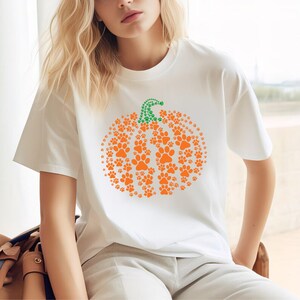 Peut inclure: T-shirt blanc avec un motif de citrouille compos&eacute; d'empreintes de pattes orange et d'une tige verte en pointill&eacute;s. Le t-shirt est de style d&eacute;contract&eacute;, id&eacute;al pour l'automne ou Halloween.