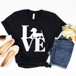 以下が含まれることがあります： LOVEという言葉の中にダックスフントの白いグラフィックが描かれた黒いTシャツです。