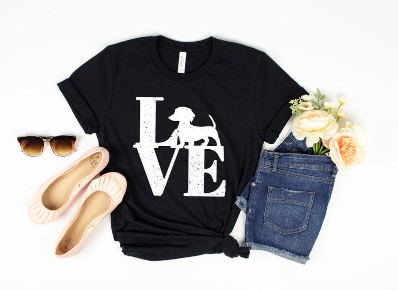 以下が含まれることがあります： LOVEという言葉の中にダックスフントの白いグラフィックが描かれた黒いTシャツです。