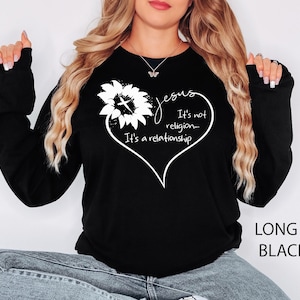 May include: A black long-sleeve sweatshirt featuring a white graphic of a sunflower with a cross in the center, shaped into a heart outline. The text reads: Jesus It's not religion... It's a relationship. The sweatshirt has a crew neckline.