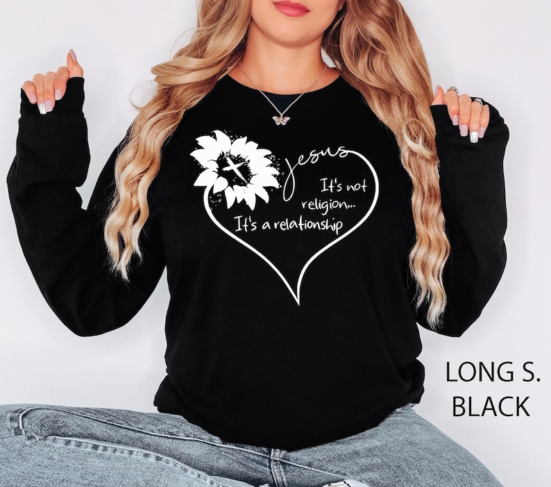 May include: A black long-sleeve sweatshirt featuring a white graphic of a sunflower with a cross in the center, shaped into a heart outline. The text reads: Jesus It's not religion... It's a relationship. The sweatshirt has a crew neckline.
