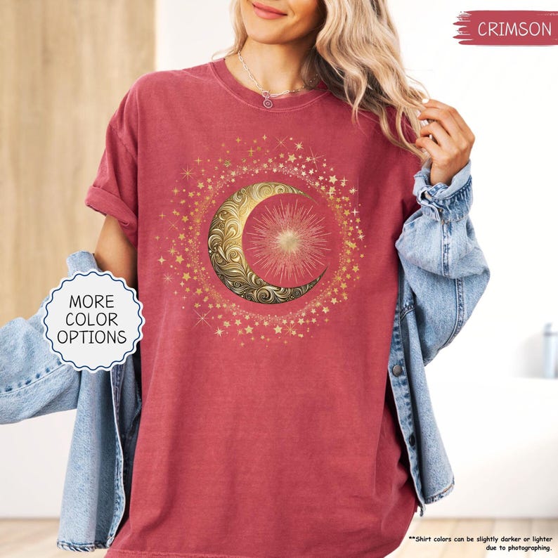 May include: Crimson-colored t-shirt featuring a gold crescent moon and sun design surrounded by stars. The shirt has rolled-up sleeves and the text "MORE COLOR OPTIONS" is visible. The shirt's color may vary slightly due to photography.