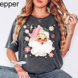 May include: Dark gray t-shirt featuring a Santa Claus graphic with a pink hat and white beard, surrounded by flowers and a peace sign. The word "Pepper" is in the top left corner.