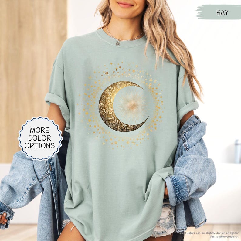May include: A light green t-shirt featuring a gold crescent moon design with intricate floral patterns and surrounding gold stars. The shirt has rolled-up sleeves and the words "MORE COLOR OPTIONS" are visible.