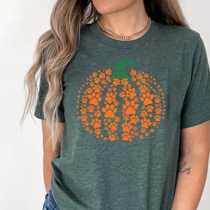 Peut inclure: T-shirt vert fonc&eacute; avec un motif de citrouille orange compos&eacute; d'empreintes de pattes. La citrouille a une tige verte. Le t-shirt est de style col rond et est fait d'une mati&egrave;re douce. Id&eacute;al pour l'automne.