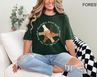 May include: A dark green t-shirt with a white circle graphic featuring hands of different skin tones clasped together. The text around the circle reads "Love Peace Humankind. Choose Kindness. Be Kind. Equality. Humans. Strong Together."