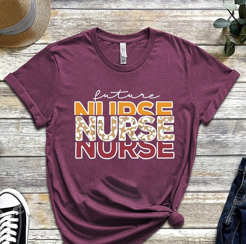 May include: A maroon t-shirt with the text "future nurse" in white, orange, and red. The word "nurse" is repeated three times, with the second instance featuring a leopard print pattern.