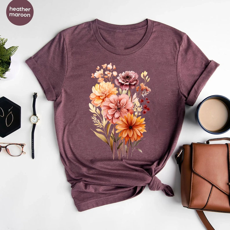 May include: A heather maroon t-shirt with a floral print featuring a bouquet of orange, pink, and brown flowers.