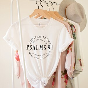 May include: White t-shirt with a black circle graphic that says "God is my refuge and my fortress, Psalms 91, I will find shelter under his wings."