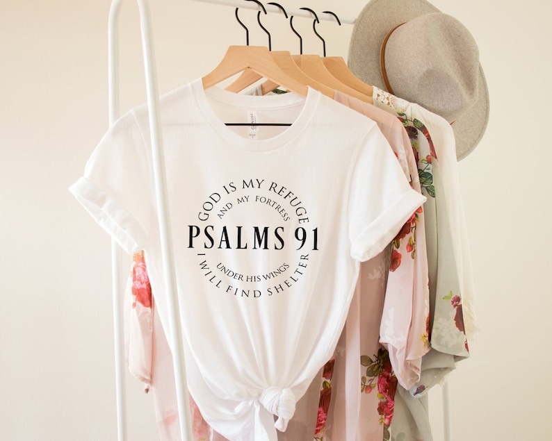May include: White t-shirt with a black circle graphic that says "God is my refuge and my fortress, Psalms 91, I will find shelter under his wings."