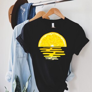 Pu&ograve; includere: Maglietta nera con una grafica di un tramonto a forma di fetta di limone. La fetta di limone &egrave; gialla e il tramonto &egrave; arancione e giallo.