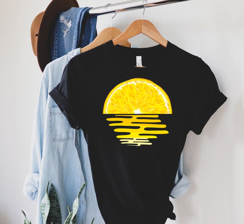 Pu&ograve; includere: Maglietta nera con una grafica di un tramonto a forma di fetta di limone. La fetta di limone &egrave; gialla e il tramonto &egrave; arancione e giallo.