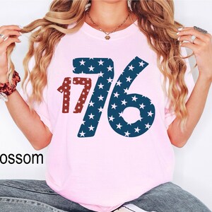 Puede incluir: Camiseta rosa con un gr&aacute;fico azul y rojo del n&uacute;mero 176 con estrellas. El n&uacute;mero est&aacute; en negrita y las estrellas son blancas.
