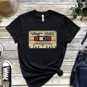 May include: Black t-shirt featuring a vintage cassette tape graphic. The tape has the text "Vintage 1986 Limited Edition" printed on it.