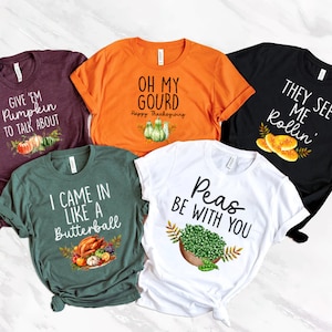 Puede incluir: Cinco camisetas diferentes con tem&aacute;tica de Acci&oacute;n de Gracias con varios dise&ntilde;os y colores. Las camisetas presentan frases como "Give 'em pumpkin to talk about", "Oh my gourd", "I came in like a butterball", "They see me rollin'" y "Peas be with you".