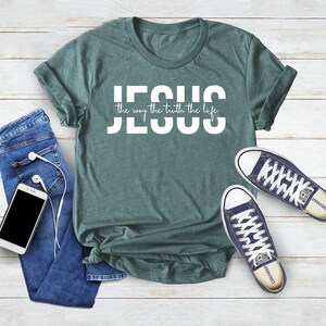 Pu&ograve; includere: Una maglietta verde acqua con la scritta "JESUS the way the truth the life" in lettere bianche.