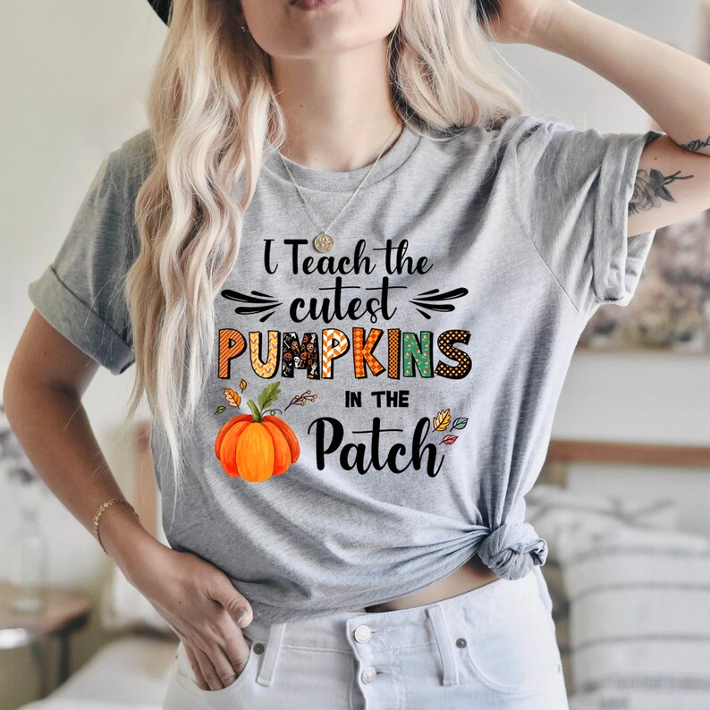 May include: A light grey t-shirt featuring the phrase "I Teach the Cutest Pumpkins in the Patch." The design includes a pumpkin and autumn leaves. The shirt is a short-sleeved crew neck.